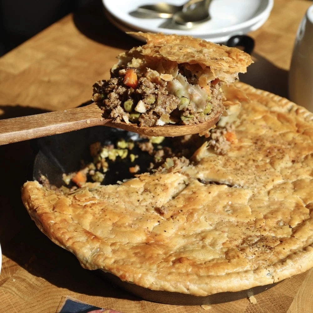 A large spoonful taken out of an Impossible Beef Pot Pit, with a top crispy plant-based crust, and savory plant-based meat, carrots and peas. 