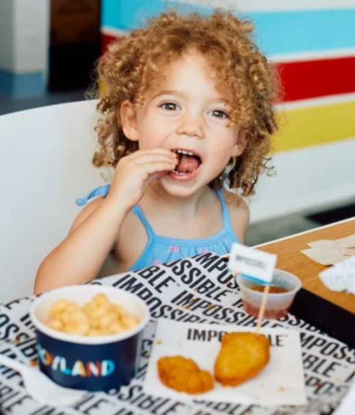 young girl eating Impossible chicken nuggets on a tray with fries and ketchup