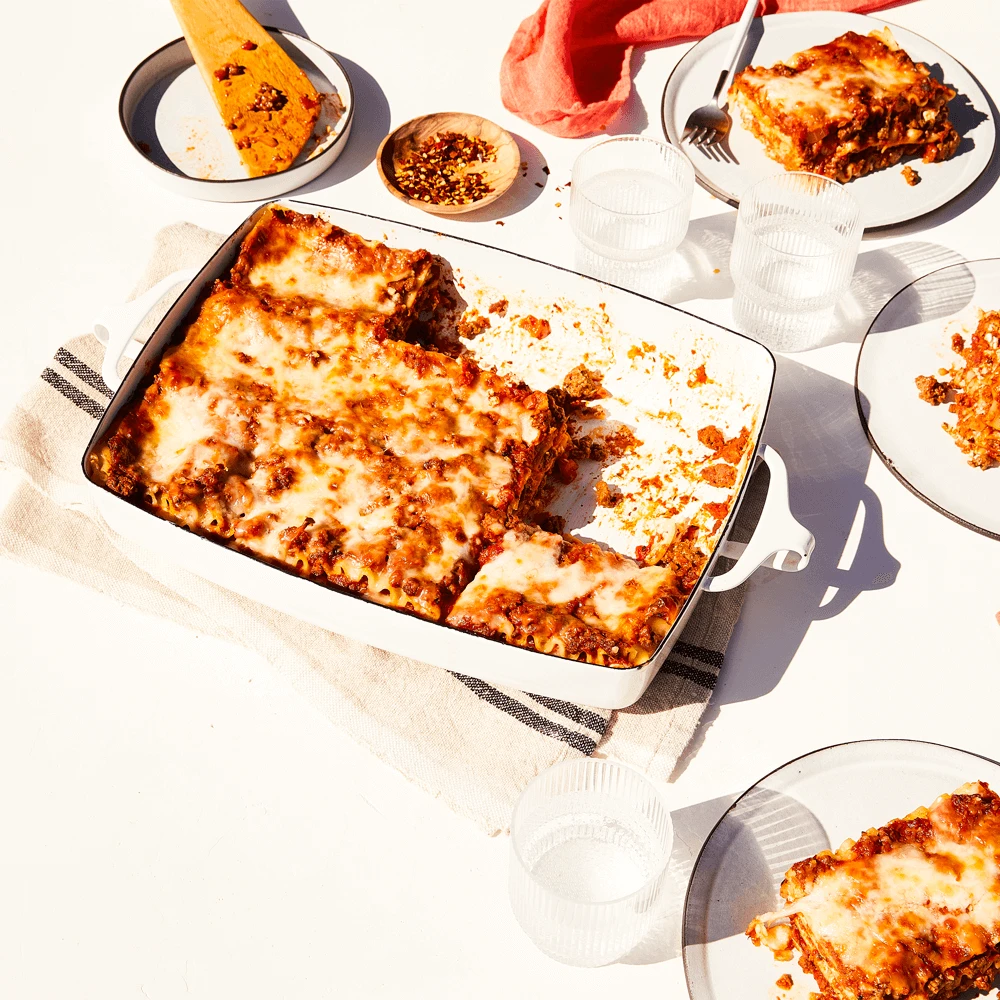 A large pan of lasagna with lots of melted cheese and a hearty Impossible Beef meat sauce, with several pieces removed and served on plates. 