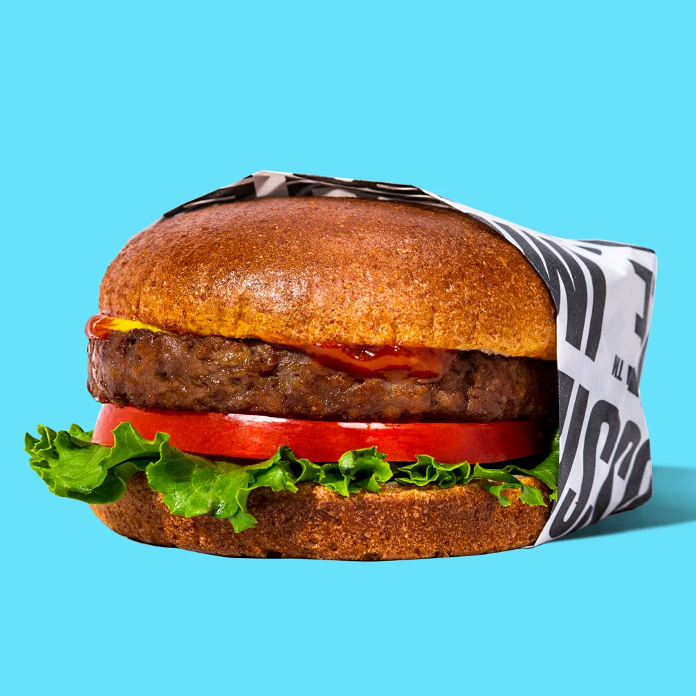 impossible burger patty with buns, ketchup, tomato and lettuce on a blue background