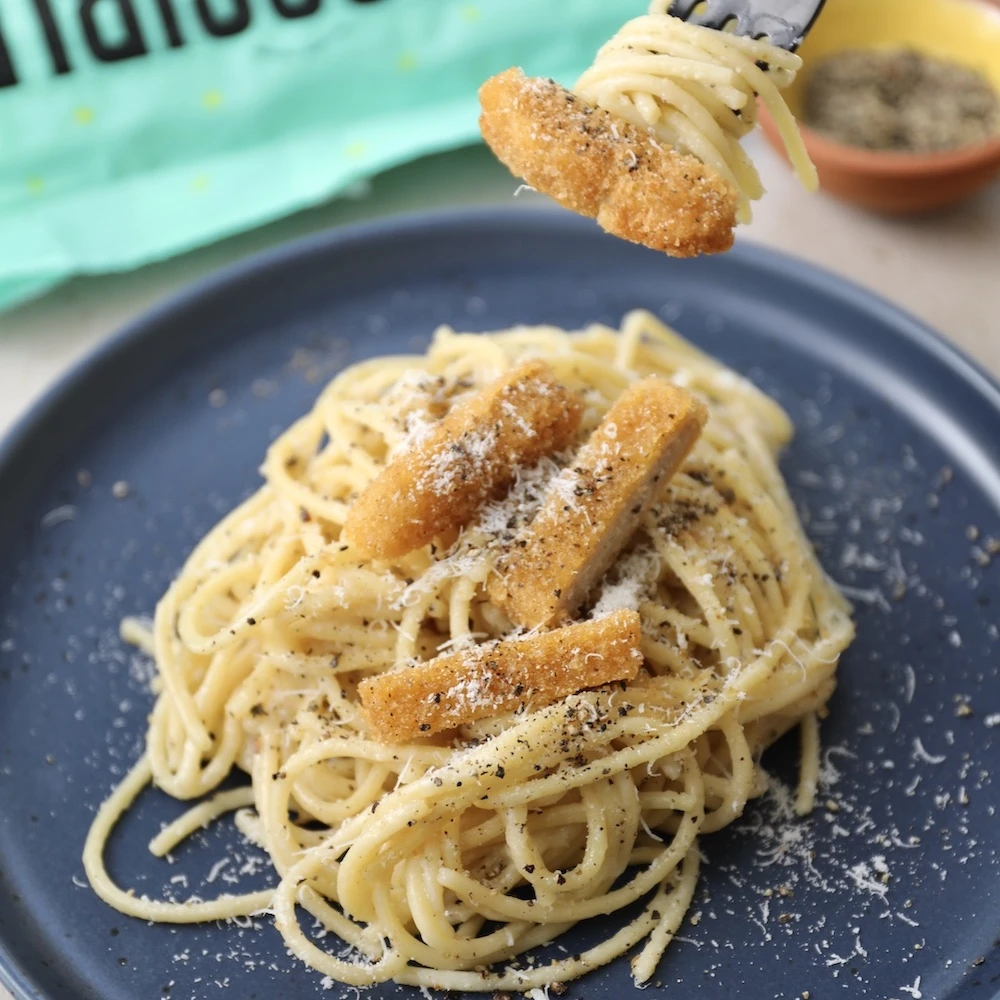 A plate of Impossible™ Chicken Nuggets Cacio e Pepe, with spaghetti, black pepper and grated cheese, topped with slices of crispy Impossible Chicken Nuggets. 