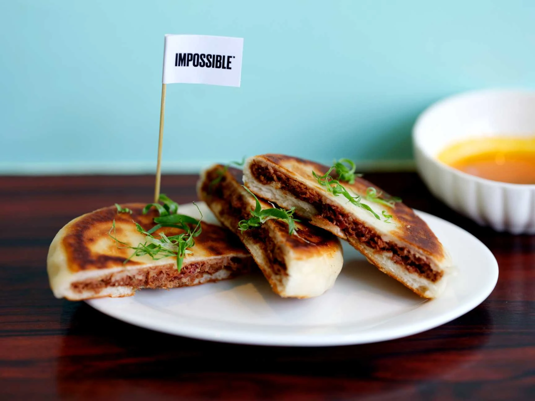 May Chow’s recipe for Impossible™ Hot Pocket with an Impossible™ flag, plated on a table with sauce in a bowl 