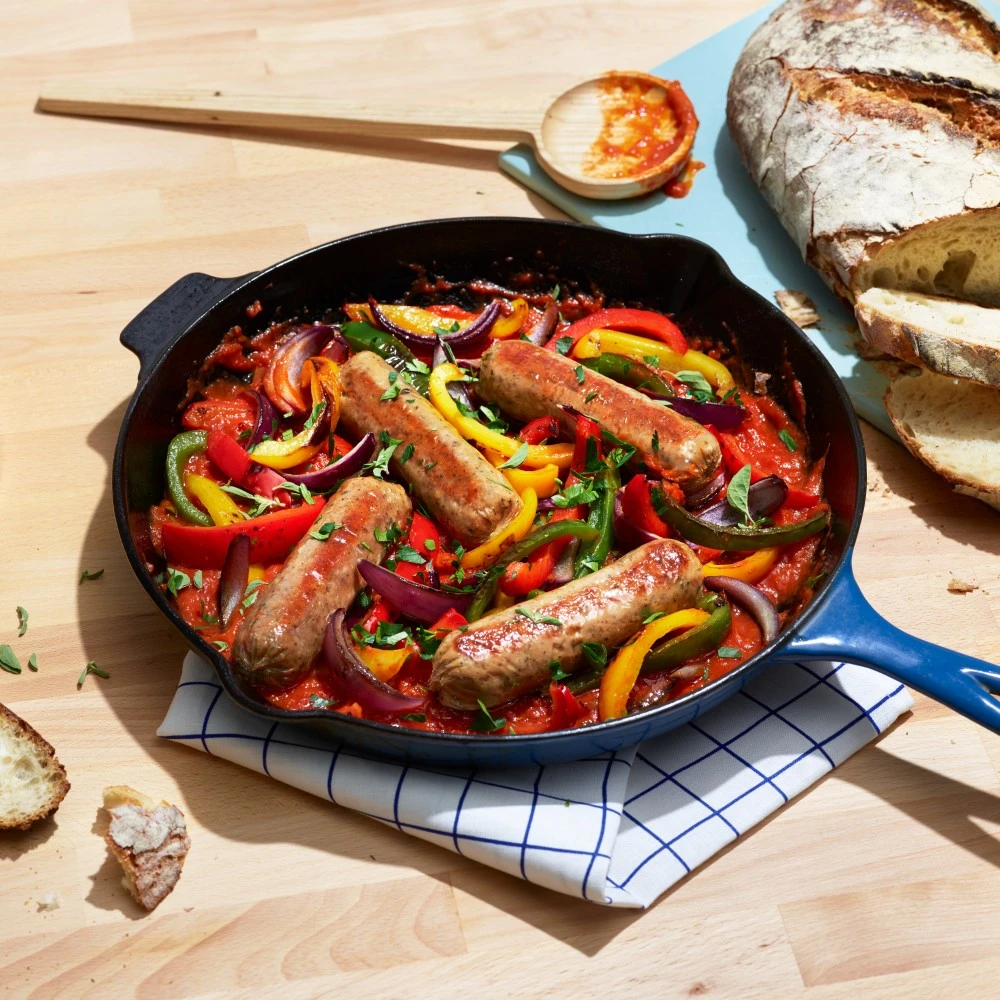 Impossible™ Italian Sausage Links in a cast iron skillet with marinara and charred peppers and onions, topped with fresh herbs and served with crusty bread. 