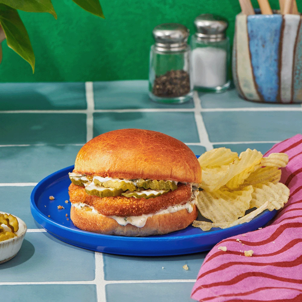 Impossible™ Classic Chicken Patty Sandwich Recipe with dill pickles and a dill pickle mayo on a soft bun, served with potato chips. 