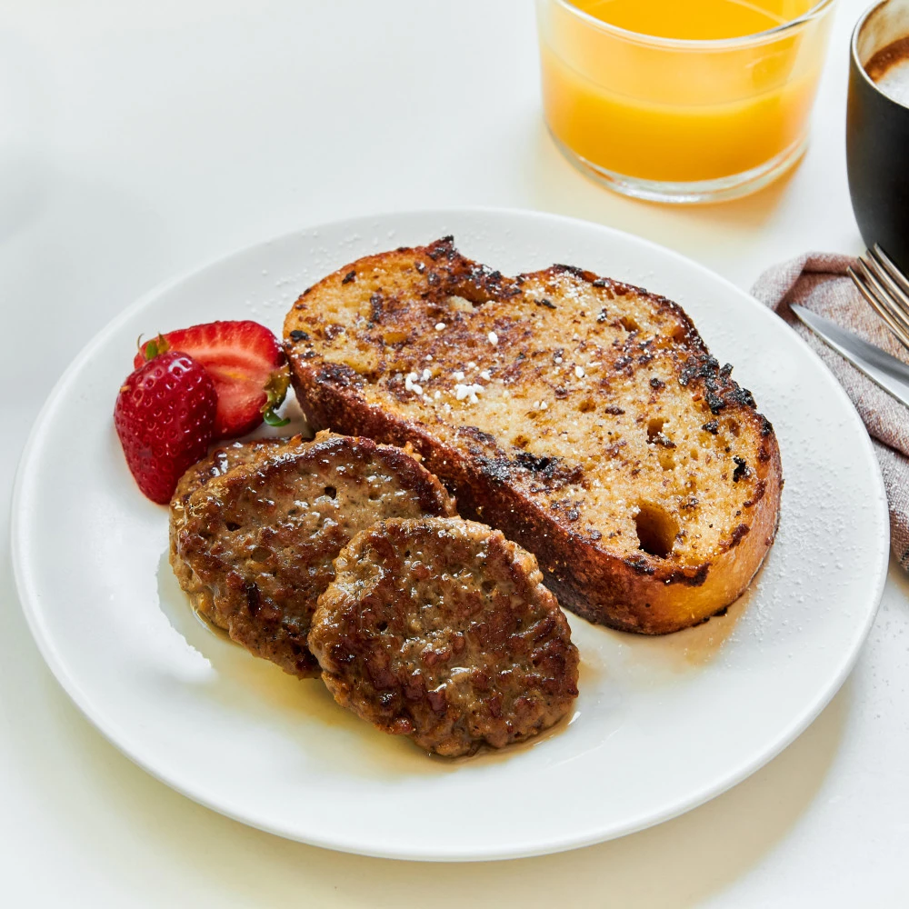 French Toast and Impossible™ Savory Sausage using meat made from plants and topped with powdered sugar, maple syrup, and strawberries.