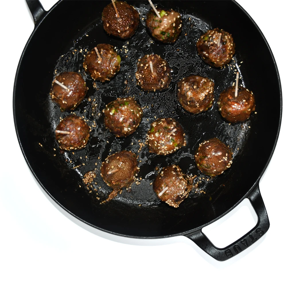 Miso-Sesame-Glazed Impossible™ Meatballs in a cast iron skillet, coated in gingery miso sauce and sesame seeds.