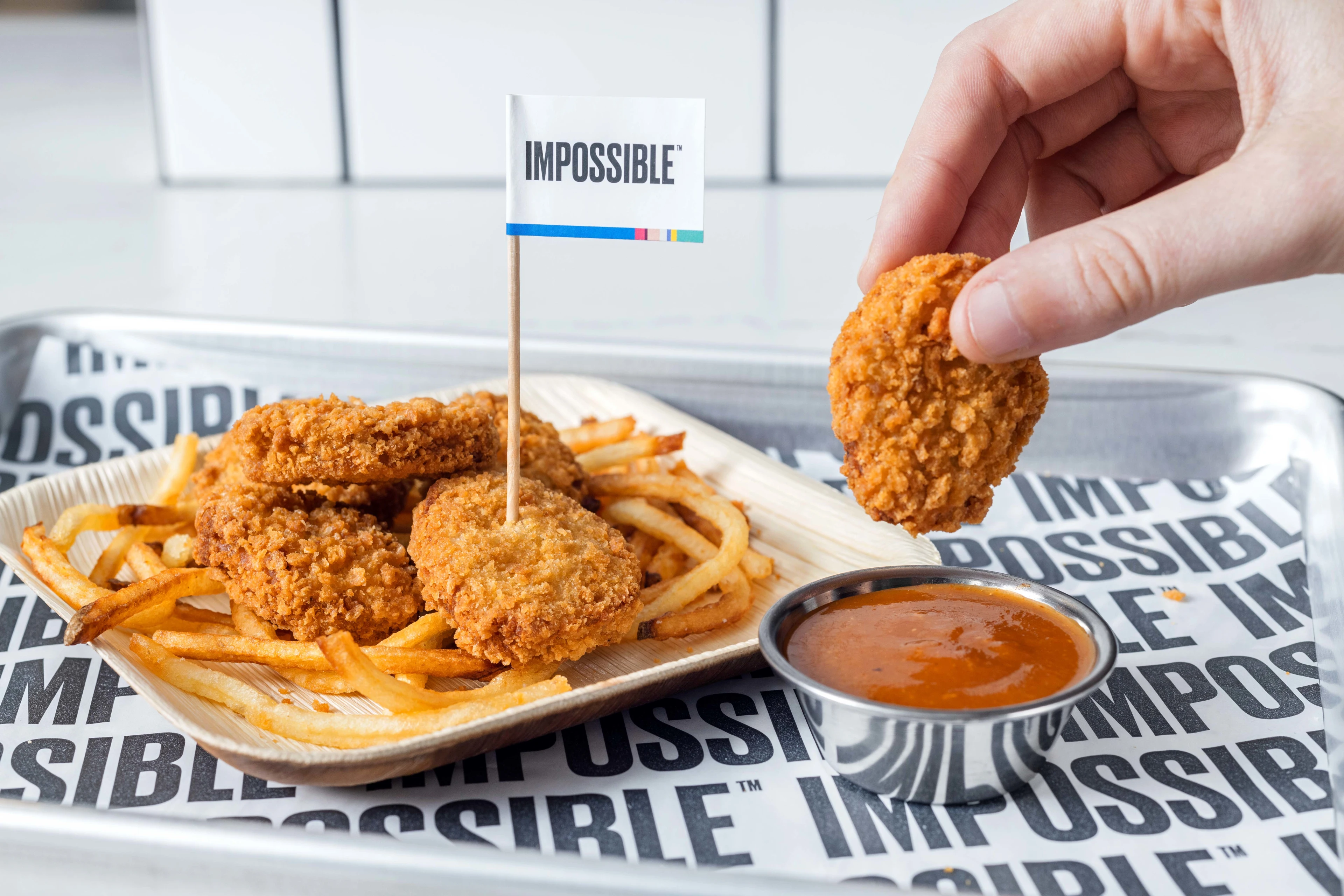 Impossible™ Chicken Nuggets being dipped into Mexican BBQ Sauce, with nuggets on a bed of Shoestring Fries