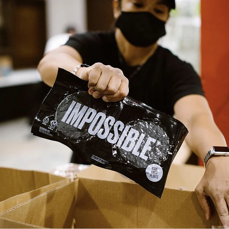 Volunteer unboxing donated Impossible Burger product at a community event. 