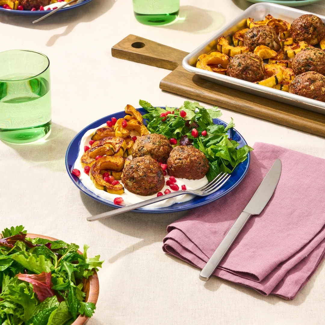 A plate of meatballs made with Impossible Ground Beef Meat From Plants atop labneh, with an herb salad and roasted delicata squash, garnished with fresh pomegranate seeds.