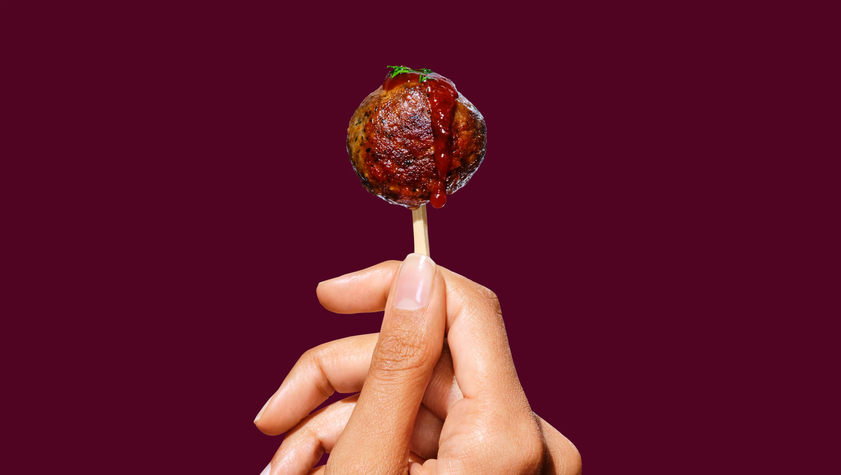 A hand holding a pick topped with an Impossible Meatball.