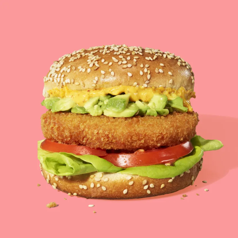 A crispy Impossible™ Chicken Patty Made From Pants on a sesame seed bun, with fresh lettuce and tomato, a tangy avocado topping and a whole grain honey mustard. 