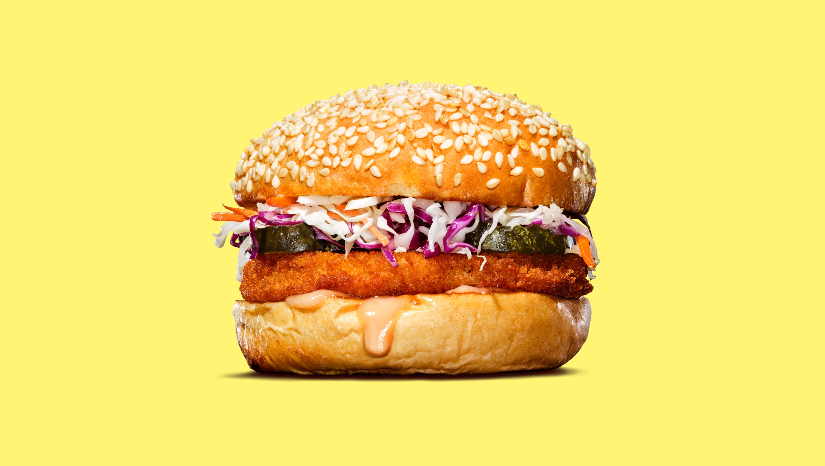 Impossible spicy chicken patty in a sandwich with slaw, pickles and a sesame bun on a yellow background
