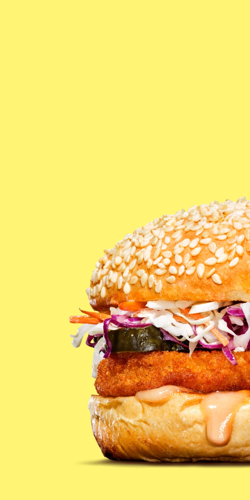 Impossible spicy chicken patty in a sandwich with slaw, pickles, sauce in a seasame bun on a yellow background