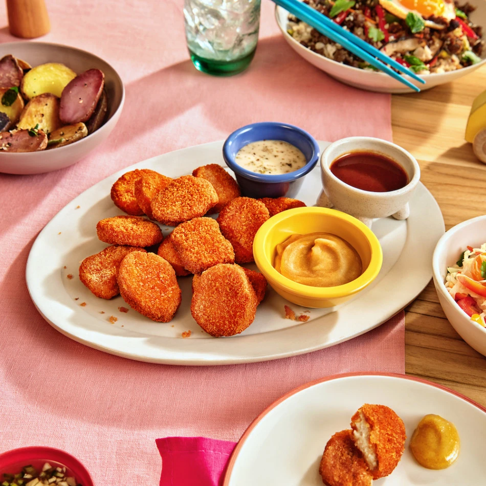A big family size plate of Impossible Spicy Chicken Nuggets Made From Plants alongside some favorite dipping sauces, and sides of coleslaw and warm potato salad. 