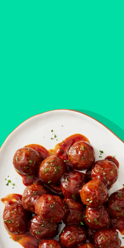 Plate of sauce covered Impossible meatballs on a green background