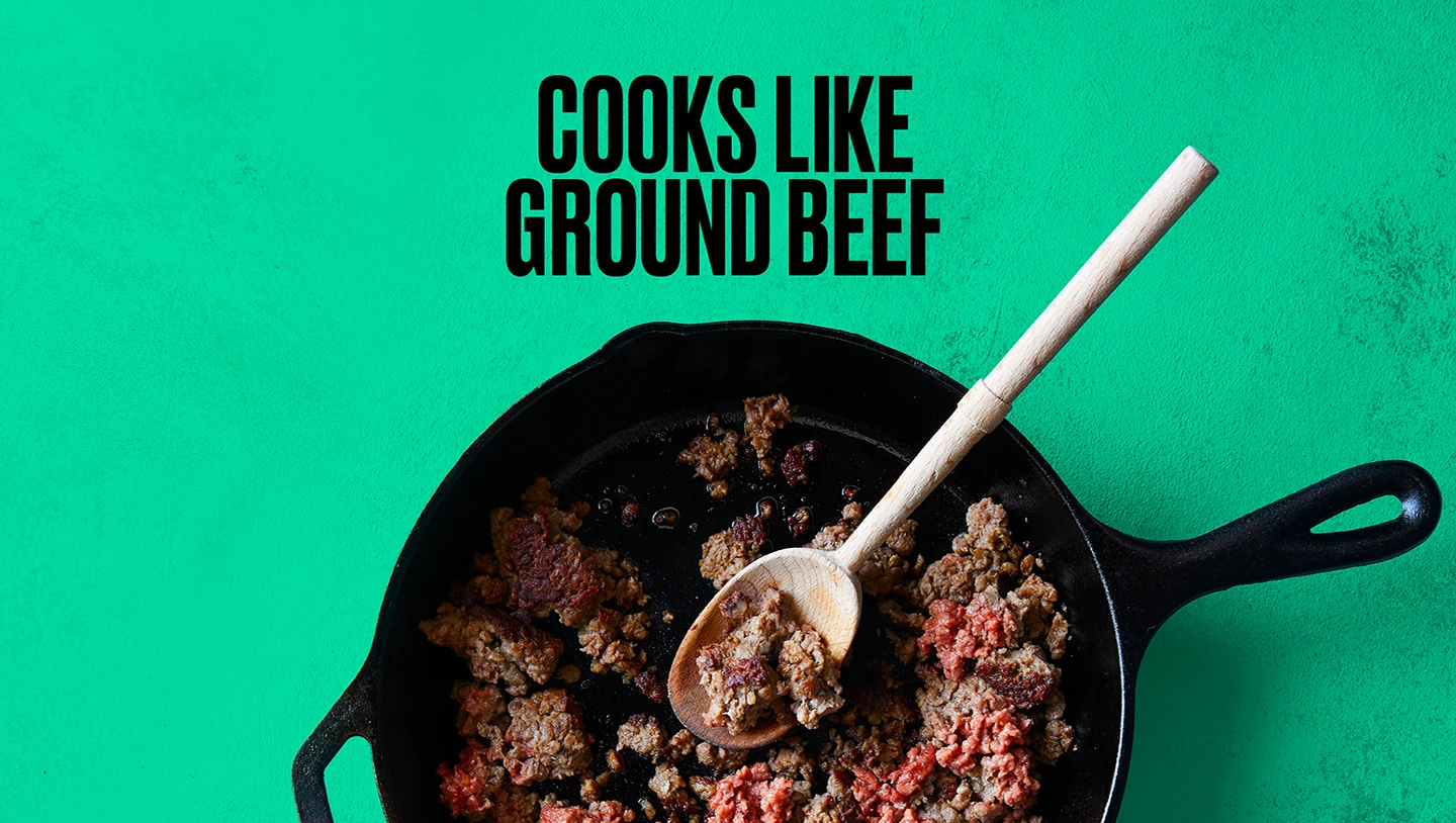 Impossible Burger cooking in a cast iron skillet with text "Cooks like Ground Beef" on green background