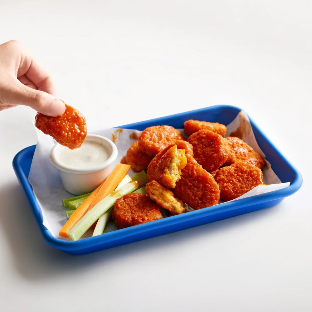 A tray with juicy Impossible Chicken Nuggets Made From Plants, coated in Buffalo Sauce, with ranch dressing for dipping and celery and carrot sticks. 