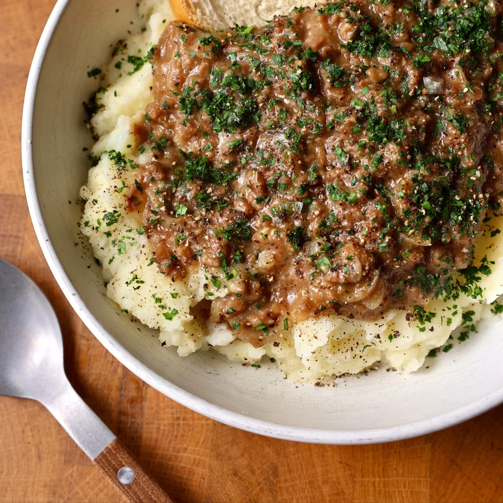 A big bowl of Impossible Thanksgiving Gravy on top of mashed potatoes and garnished with finely chopped parsley. 