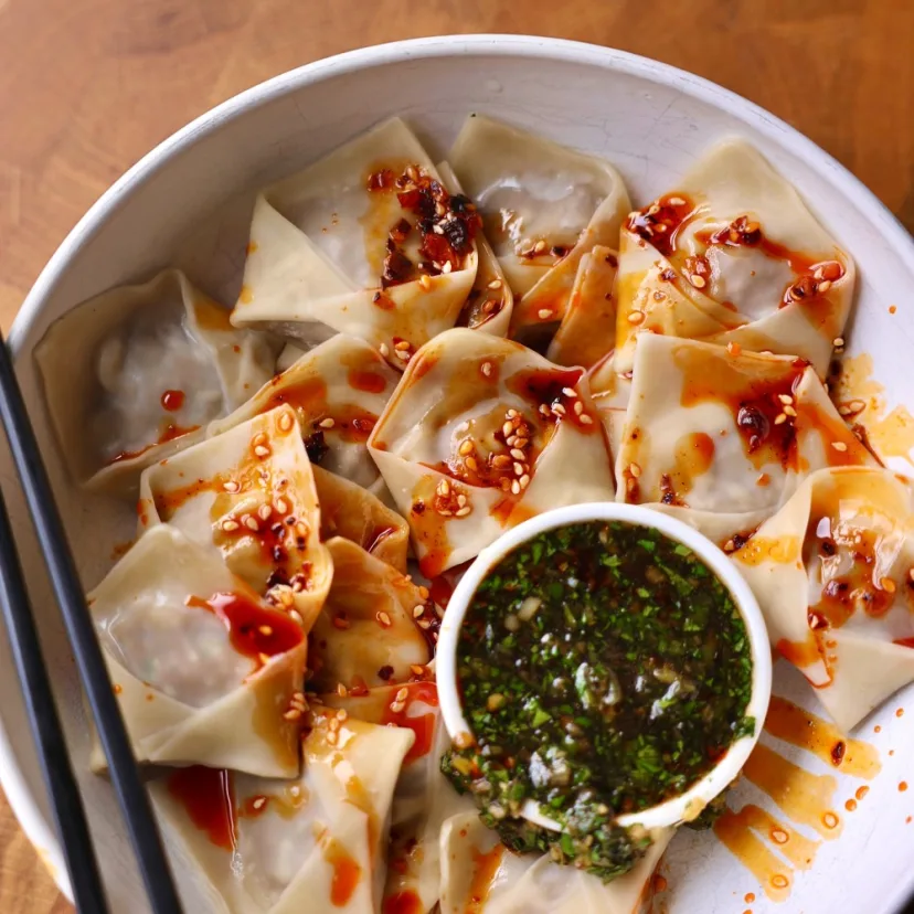 Impossible™ Beef Dumplings in a bowl drizzled with chili crisp and with a charred scallion dipping sauce. 