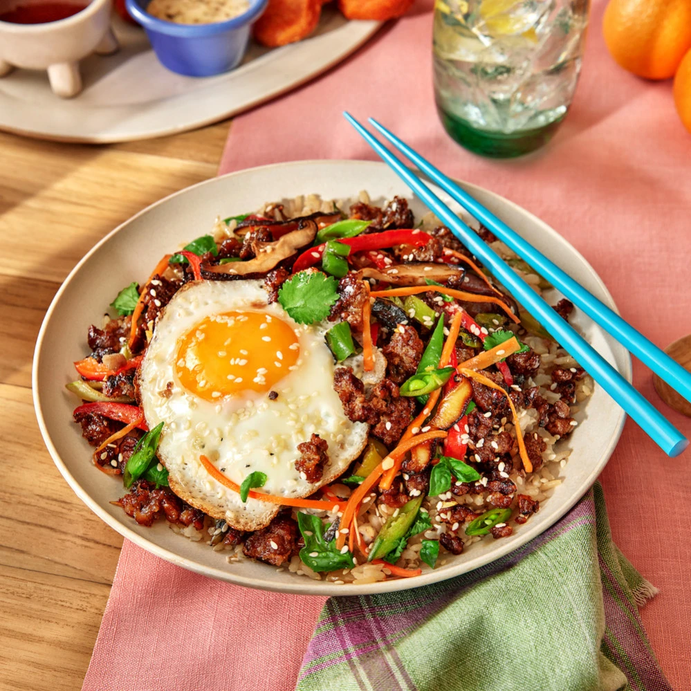 A bowl of Impossible Beef Stir Fry with a fried egg and chopsticks. 