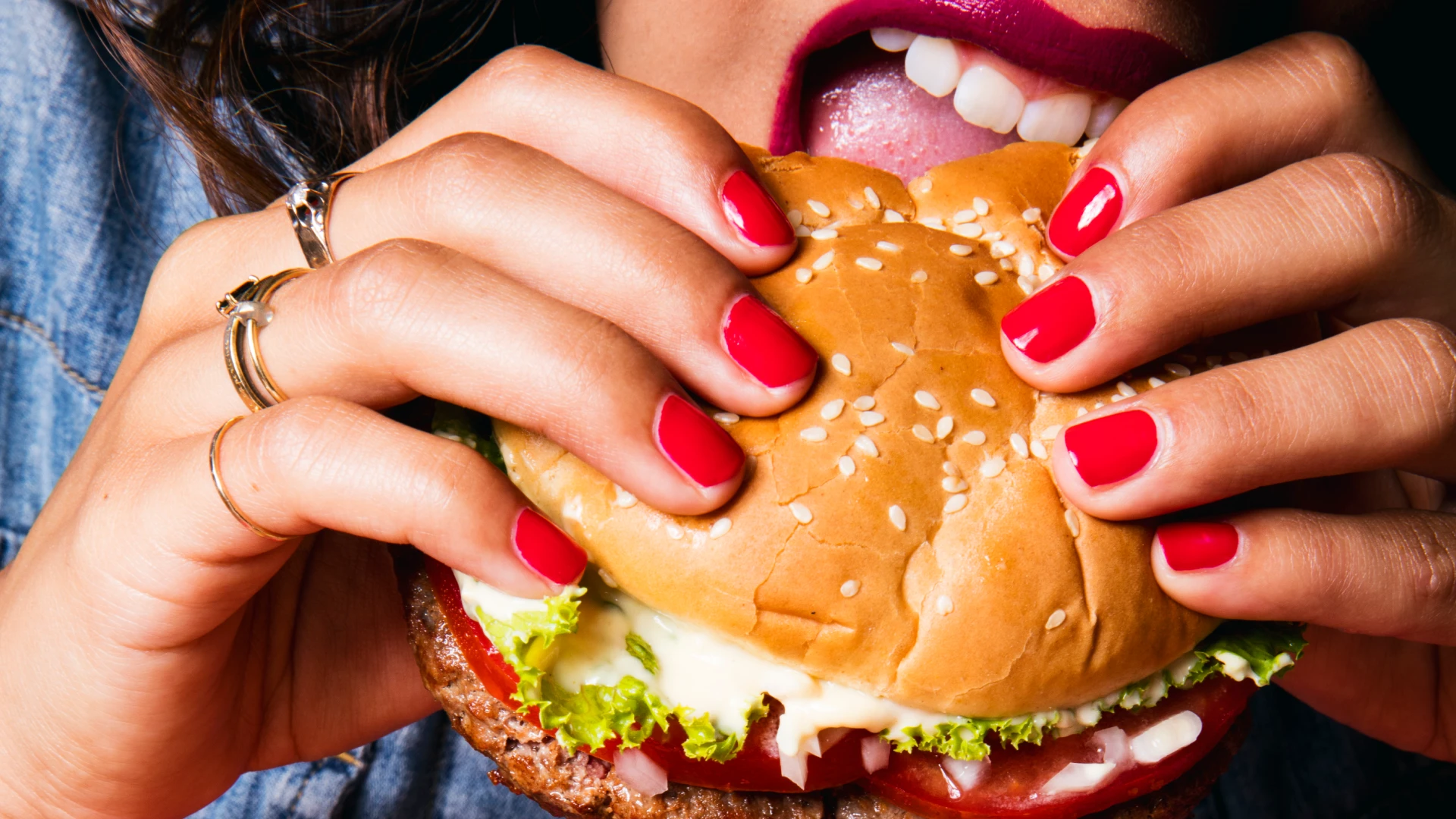 A woman eating an Impossible™ Burger sandwich with lettuce, tomato, onions, and melty cheese.