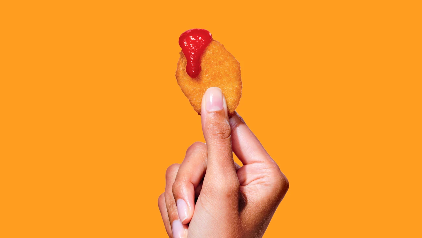 Close-up of a hand holding an Impossible Chicken Nugget dipped in ketchup.