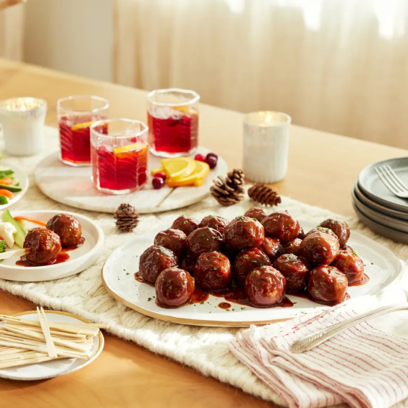 Impossible™ Holiday Appetizer Meatballs in BBQ sauce with cocktail toothpicks and holiday decor.