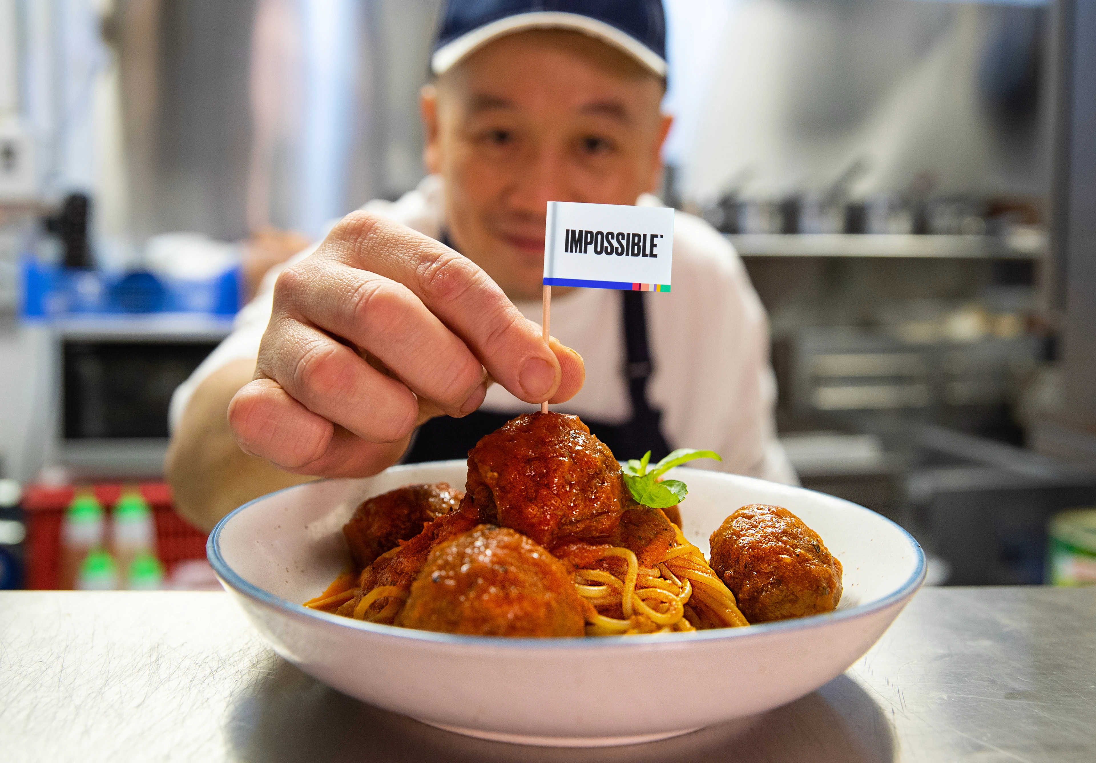 Chef placing an Impossible toothpick flag on top of Impossible spaghetti and meatballs dish back of house