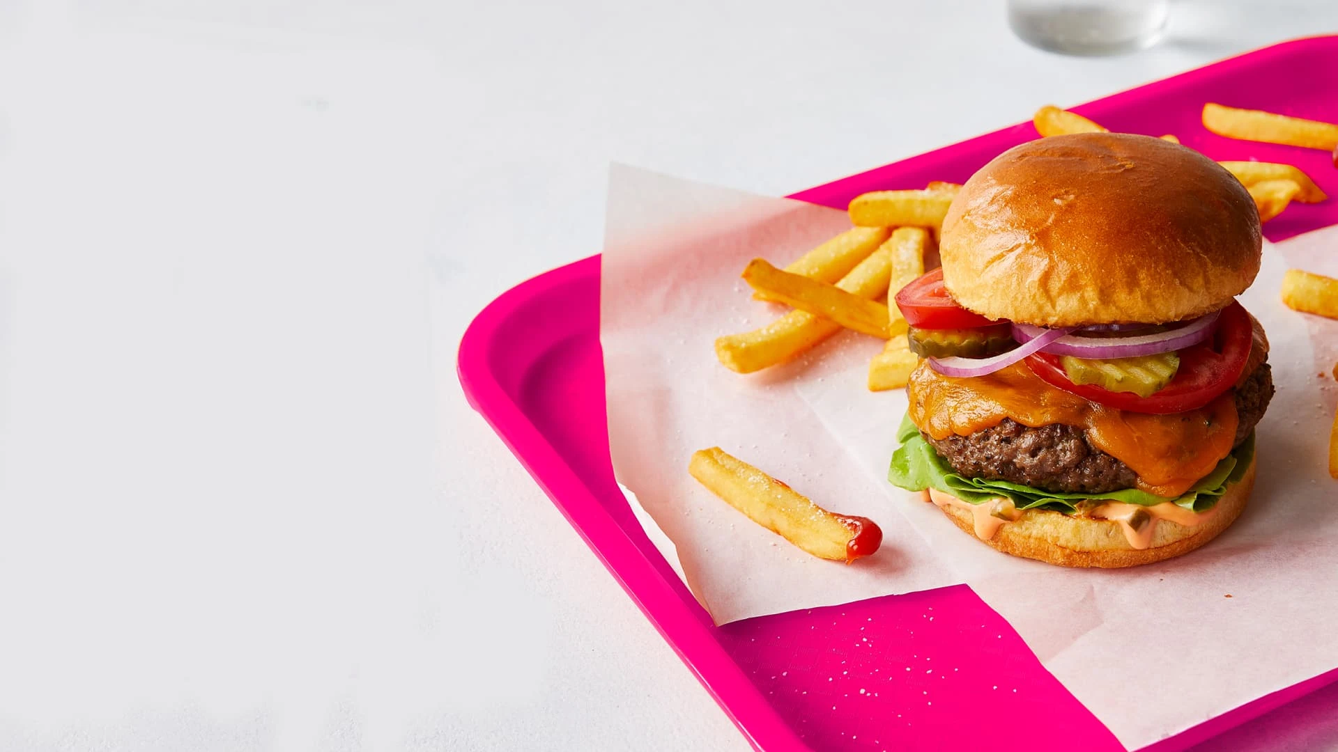 Impossible Burger with cheese, pickles, onions, tomatoes and fries and ketchup on a red tray