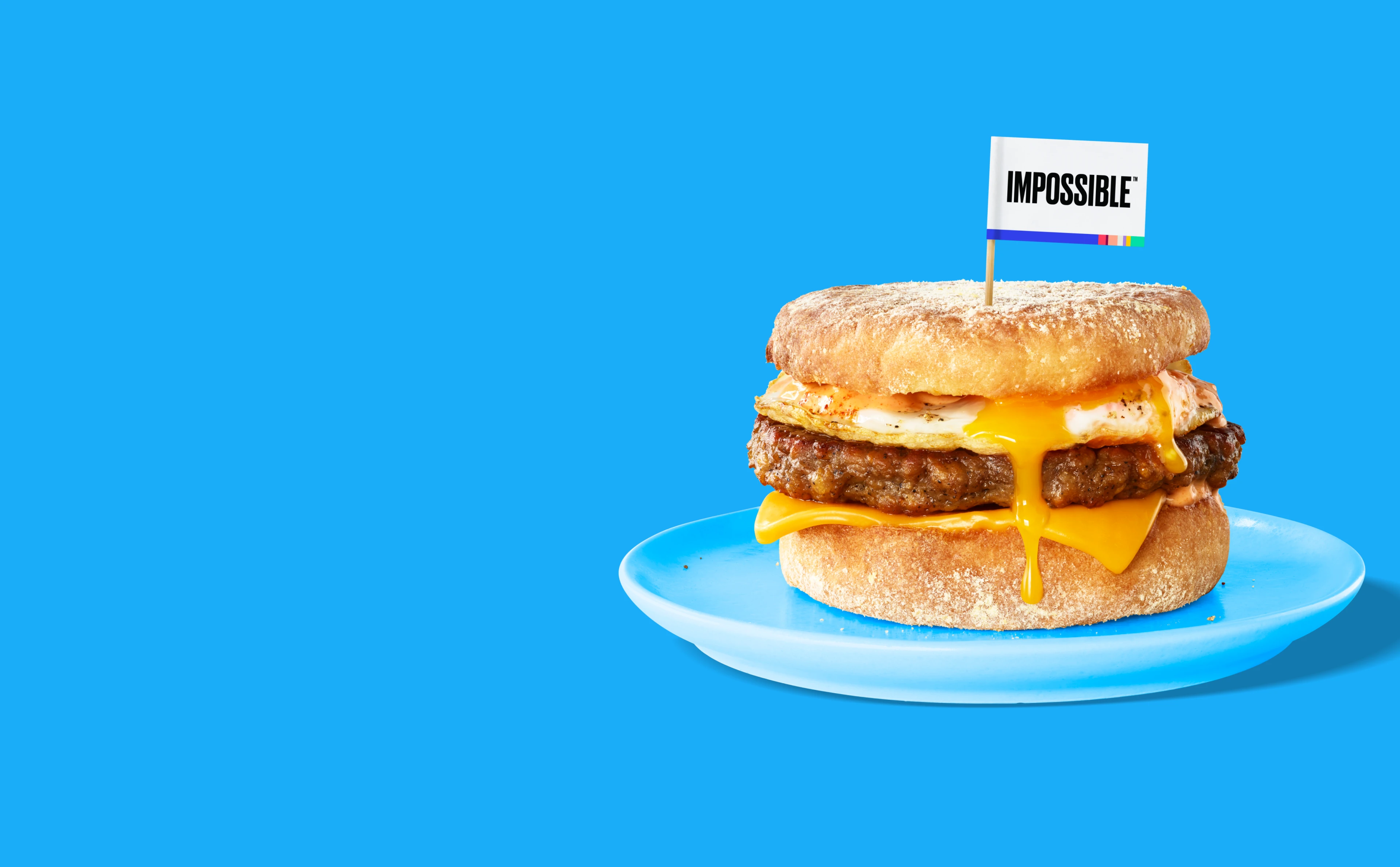 An Impossible Sausage breakfast sandwich dripping with egg and cheese on a blue plate and blue background