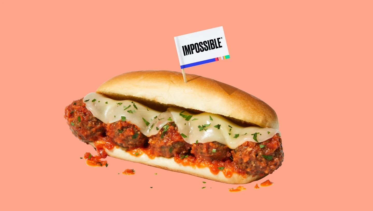 Impossible meatball sub with cheese and an impossible toothpick flag on a pink background