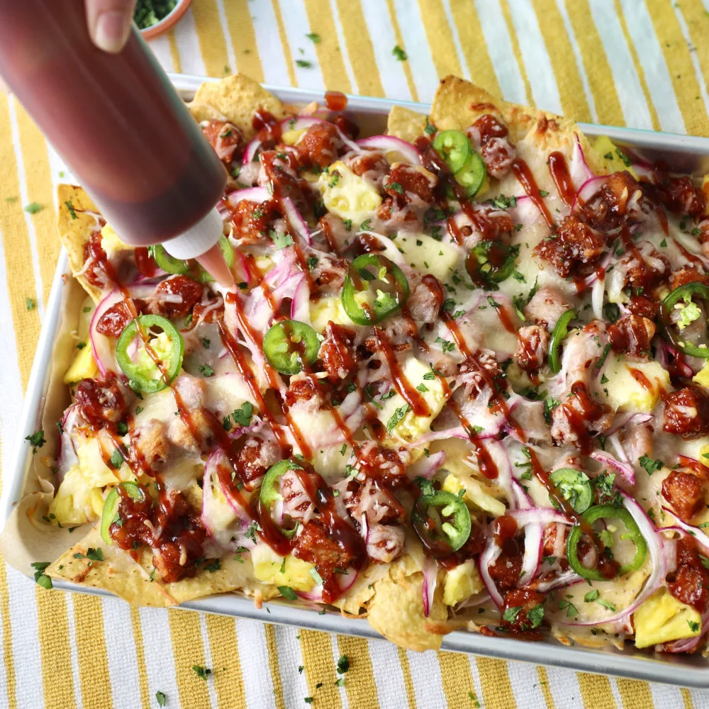 A sheet pan full of Impossible™ BBQ Chicken Nugget Nachos with tortilla chips layered with cheese and Impossible Chicken Nuggets, jalapeños and bbq sauce. 