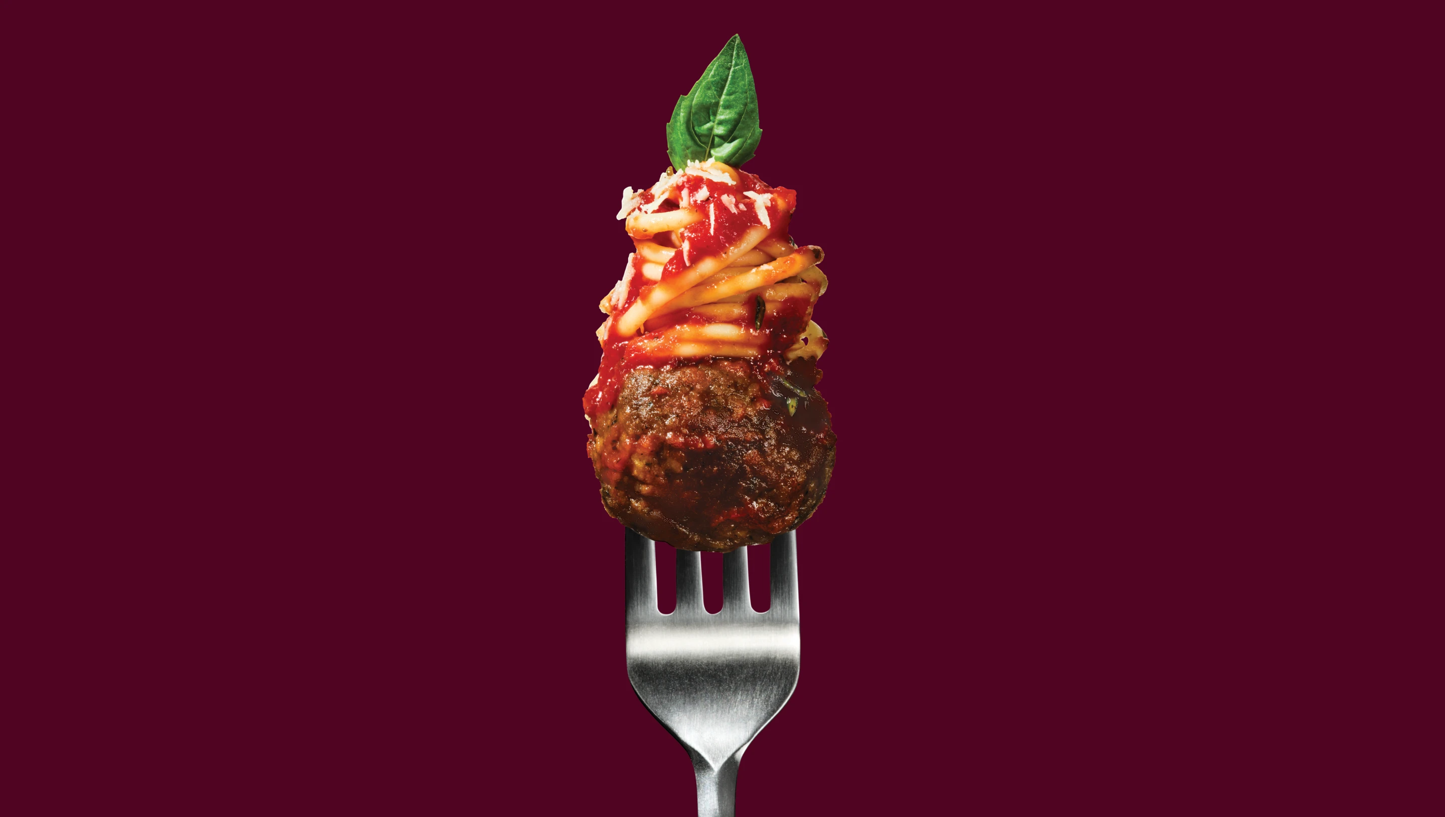 A fork holding an Impossible Meatball topped with spaghetti and basil.