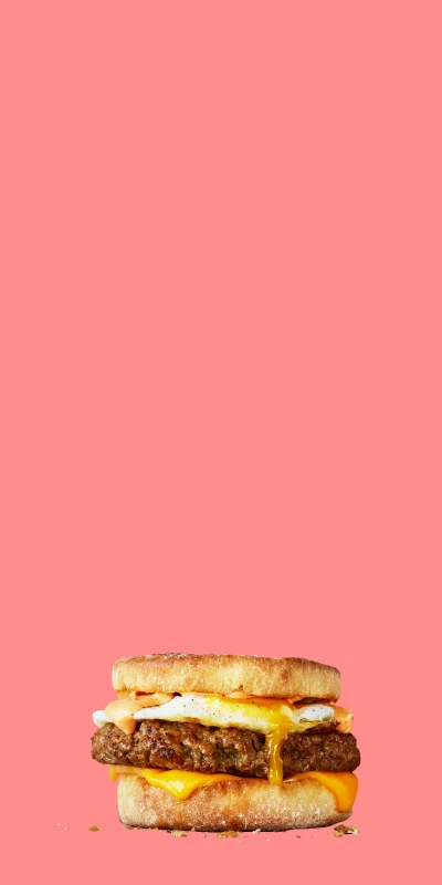 Stack of delicious food items made with Impossible Sausage made from plants including a breakfast sandwich, omelet, and breakfast burrito -- on on a pink background