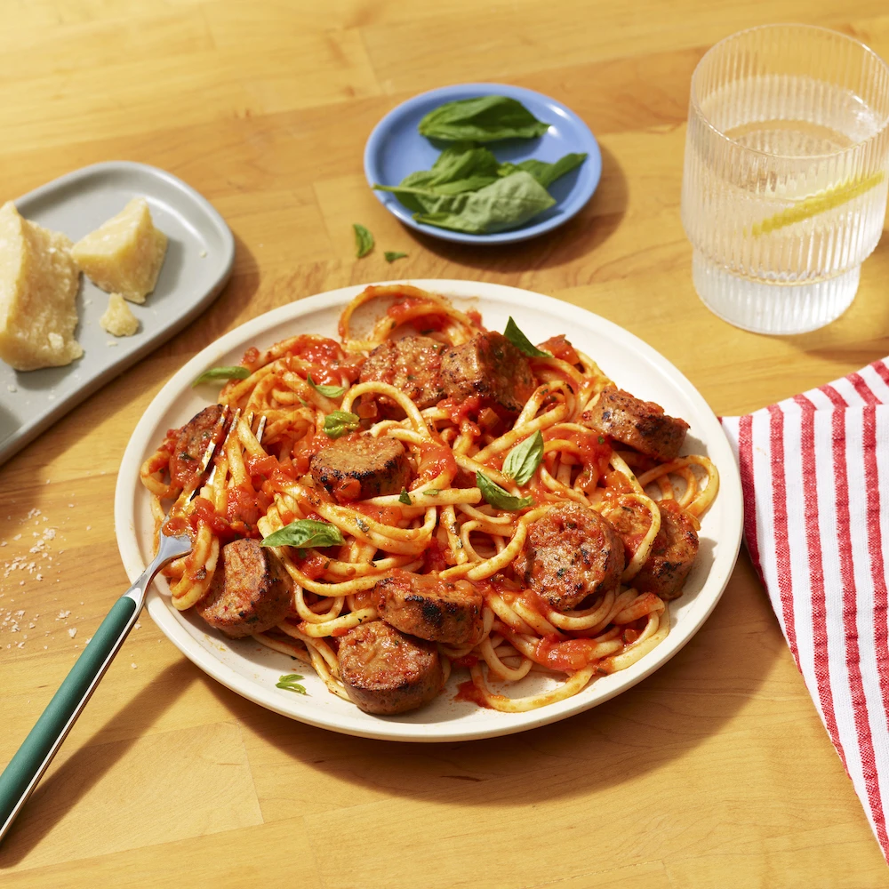 Impossible Spicy Sausage Links, cut up and mixed into zesty marinara sauce and spaghetti, served on a plate. Topped with herbs and grated parmesan cheese. 