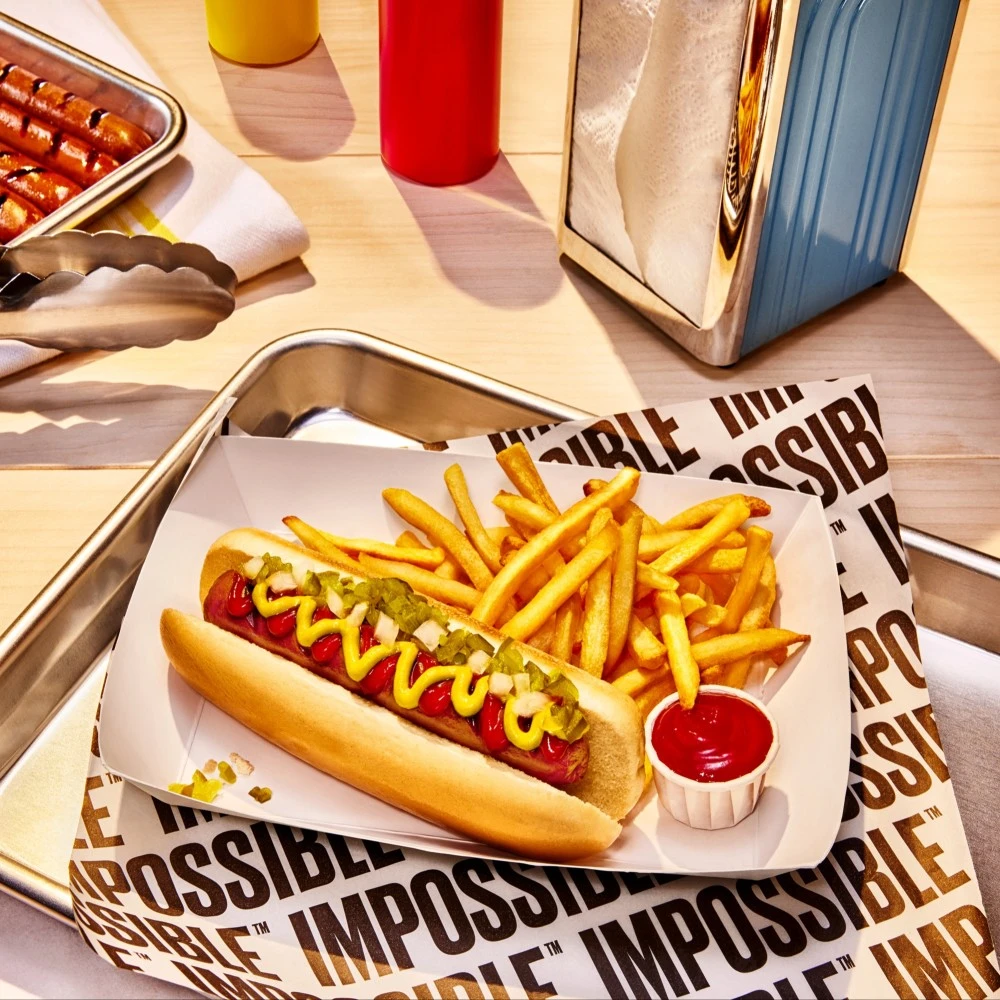 An Impossible™ L.A. Dog topped with ketchup and mustard, chopped onions and relish, with a side of fries. 