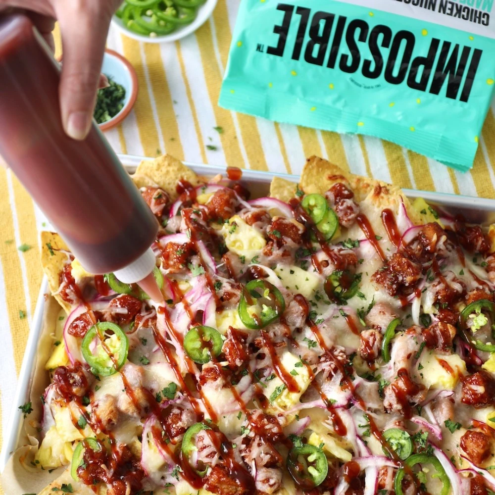 A sheet pan full of Impossible™ BBQ Chicken Nugget Nachos with tortilla chips layered with cheese and Impossible Chicken Nuggets, jalapeños and bbq sauce. 