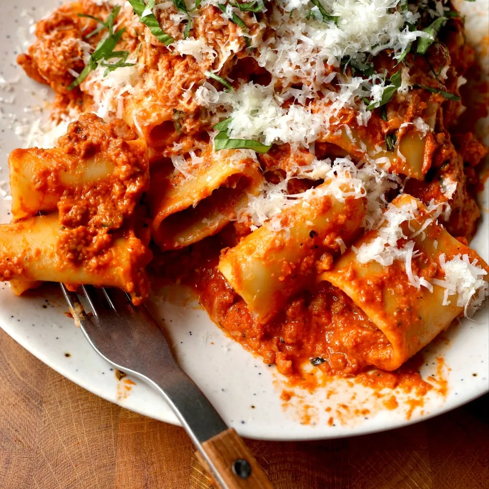 A bowl of Impossible Beef Vodka Sauce Pasta with parmesan cheese and herbs. 