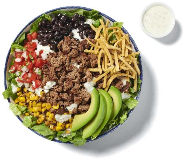 Rubio’s Impossible™ Taco Salad in a bowl using Impossible™ Burger, shredded cheese, veggies and a small cup of Ranch dressing