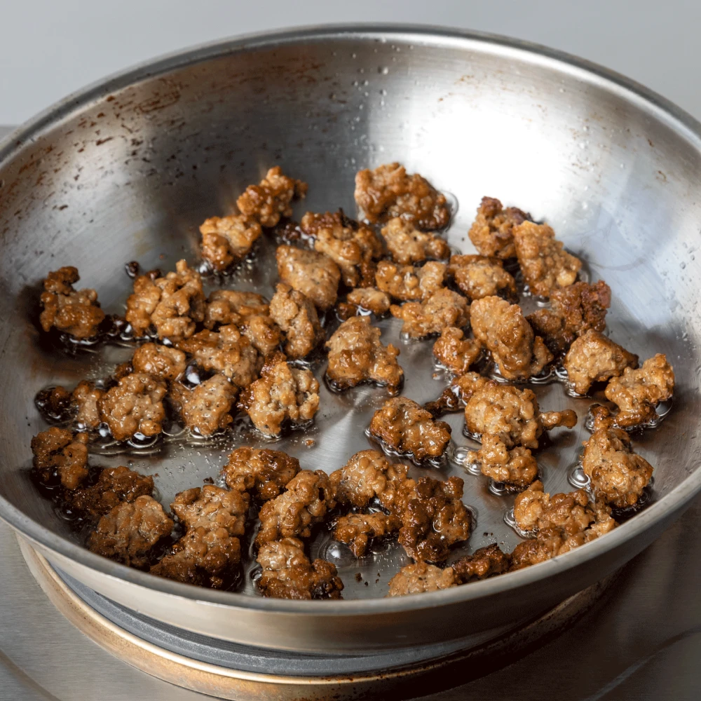 Impossible sausage crumbles cooking in a stainless steel pan
