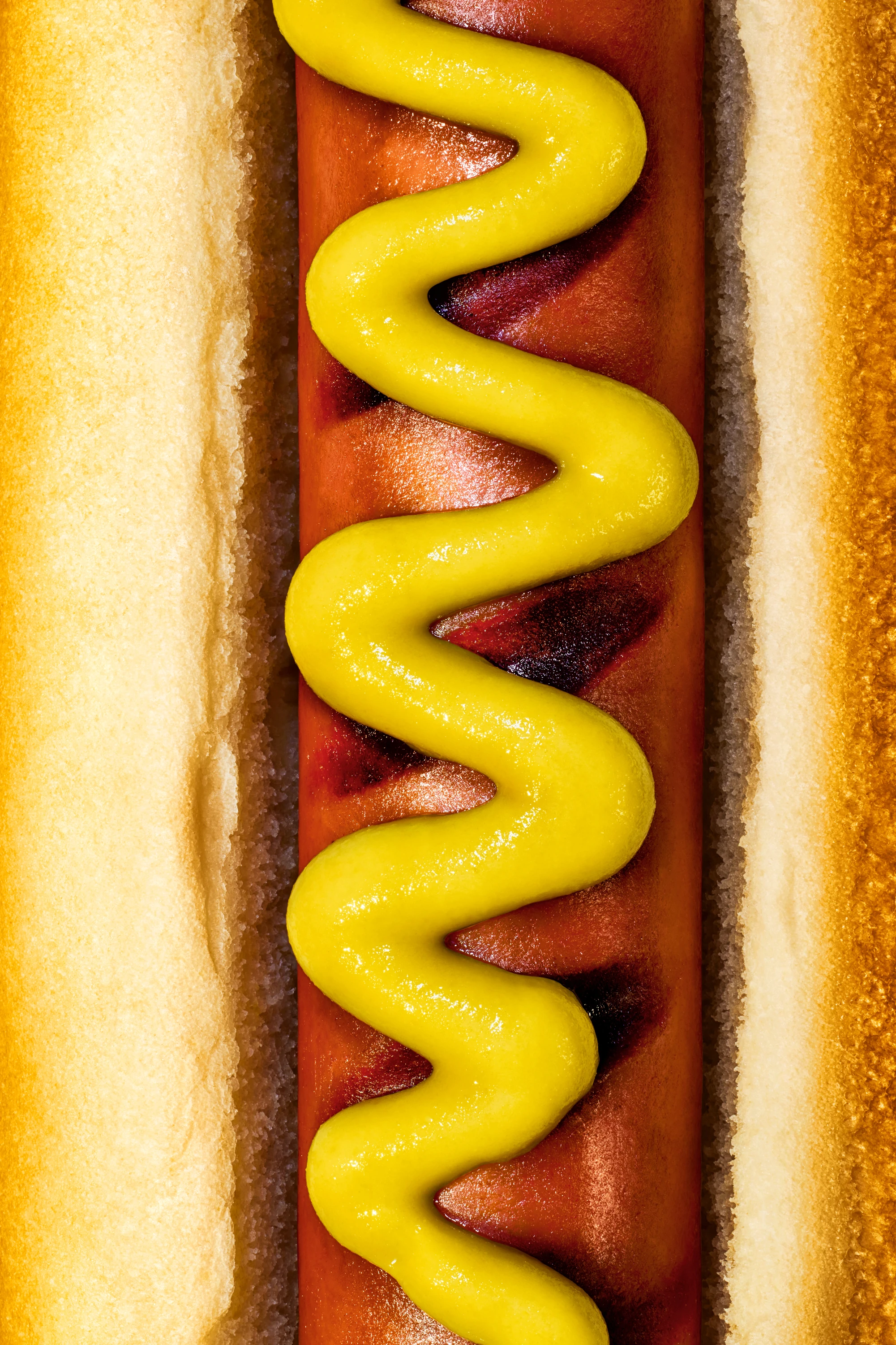 Close up picture of hot dog in bun with mustard zig zagged on the hot dog