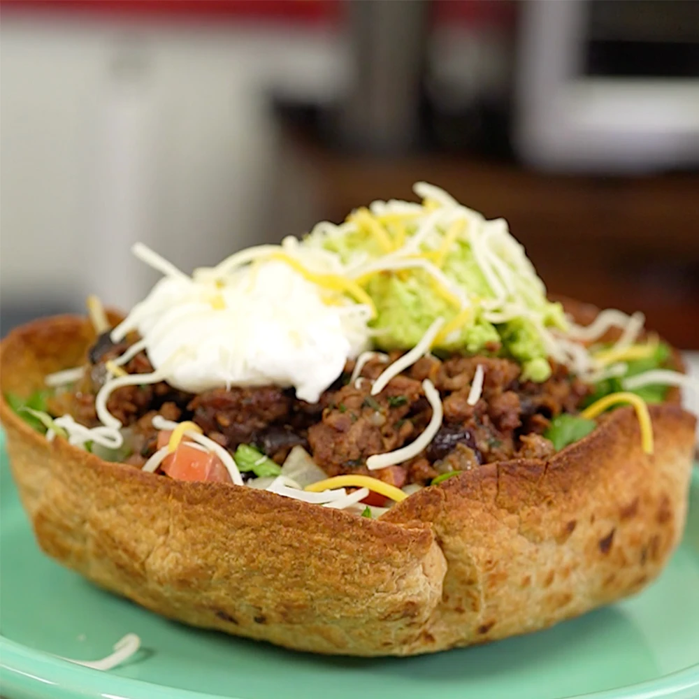 FitMenCook's Impossible™ Taco Salad made with Impossible Beef, black beans, pico de gallo and avocado, topped with sour cream and shredded cheese. 