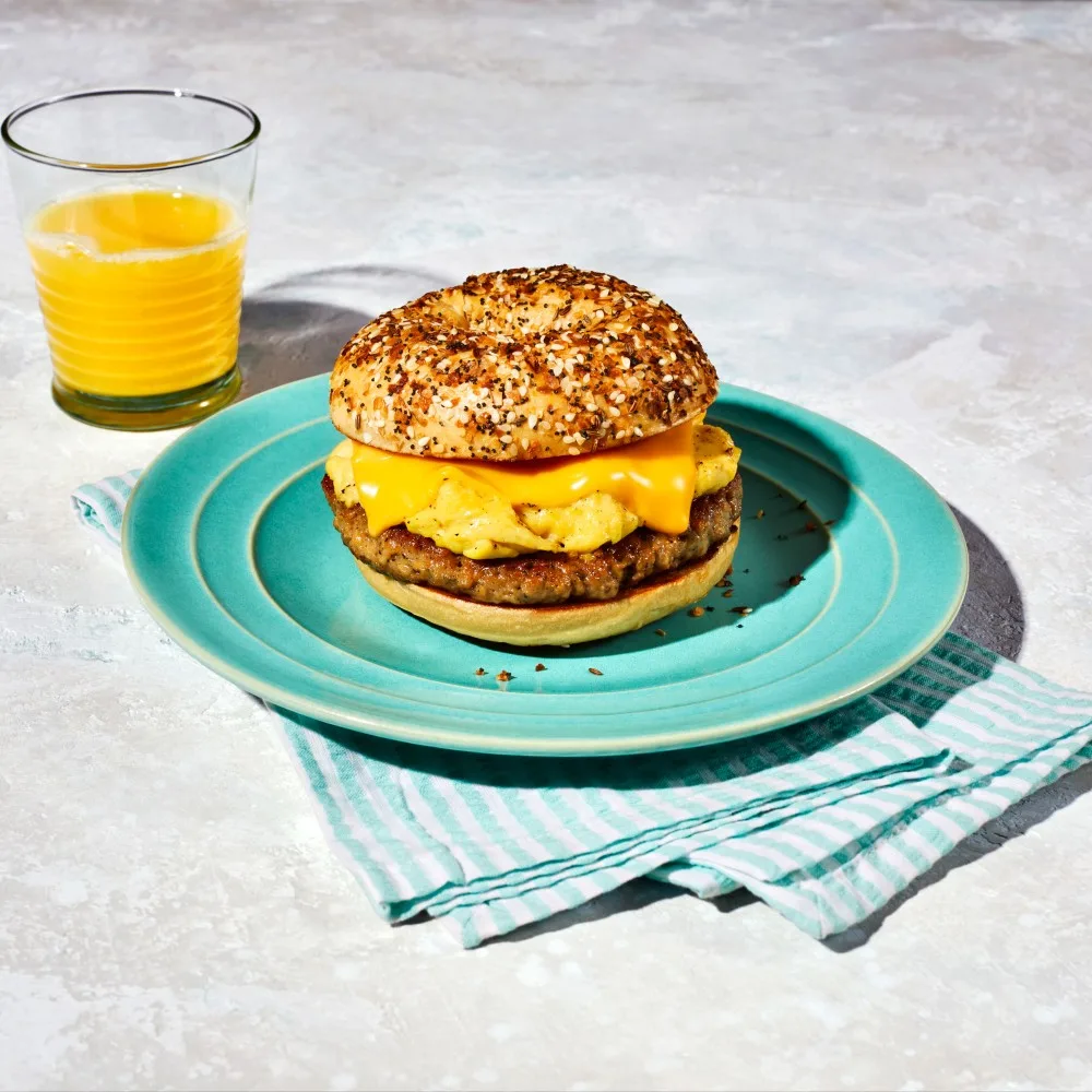 An Impossible Ground Sausage Breakfast Sandwich with scrambled eggs and melted cheese, on an everything bagel. 