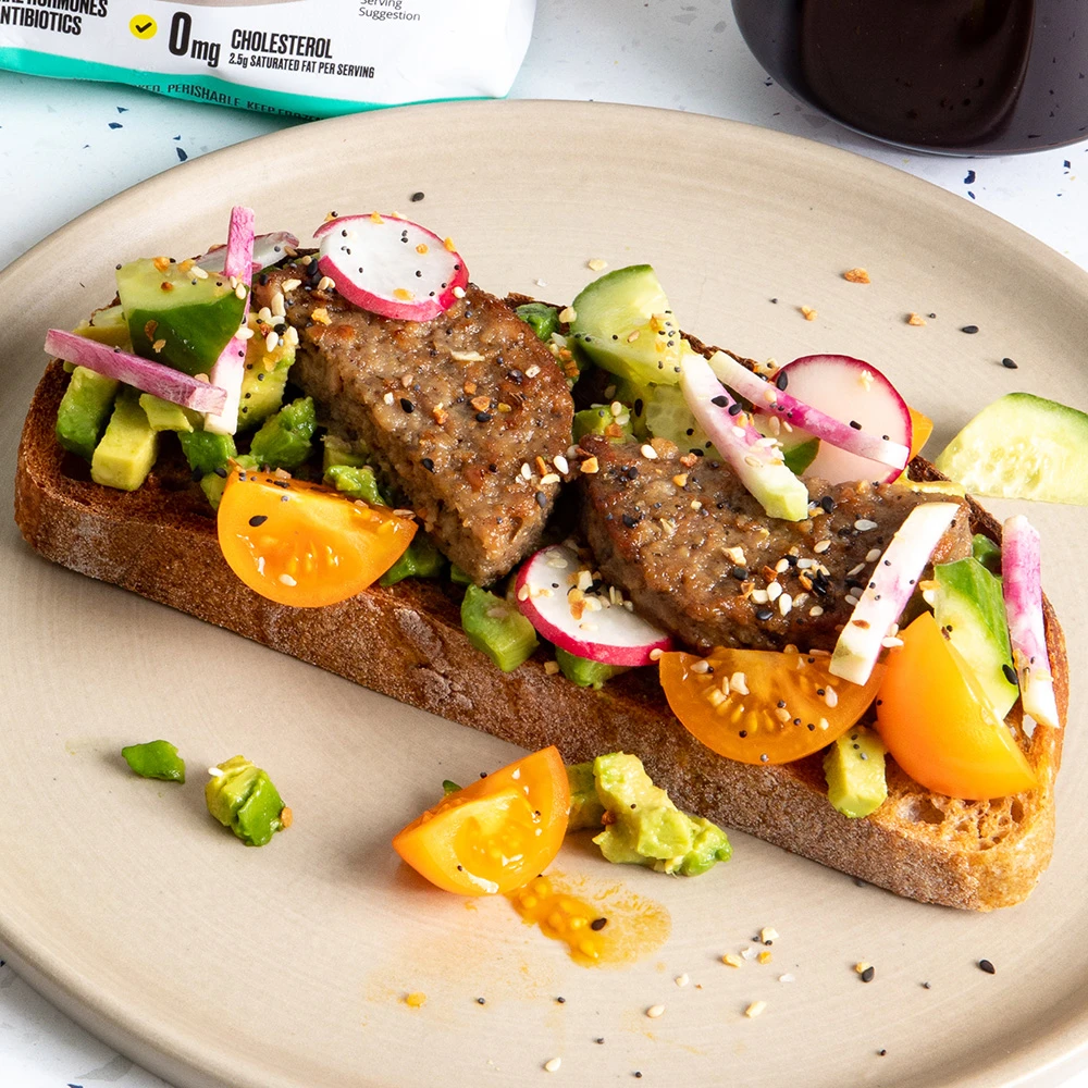 A thick slice of rustic bread piled high with avocado, sliced sungold tomatoes, fresh radishes and sliced Impossible Sausage Patties, and sprinkled with everything bagel seasoning. 