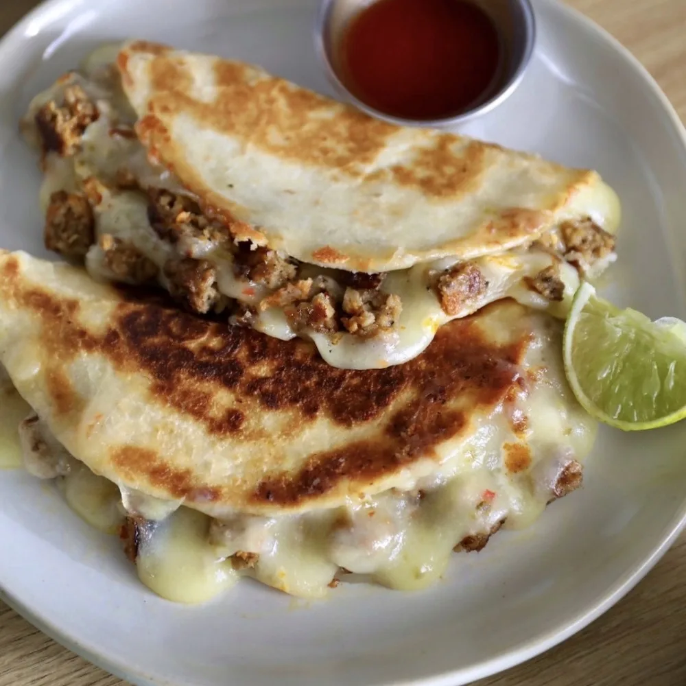 Two Impossible Sausage Patty quesadillas on a plate with melted cheese, crispy tortillas and a side of hot sauce and lime. 