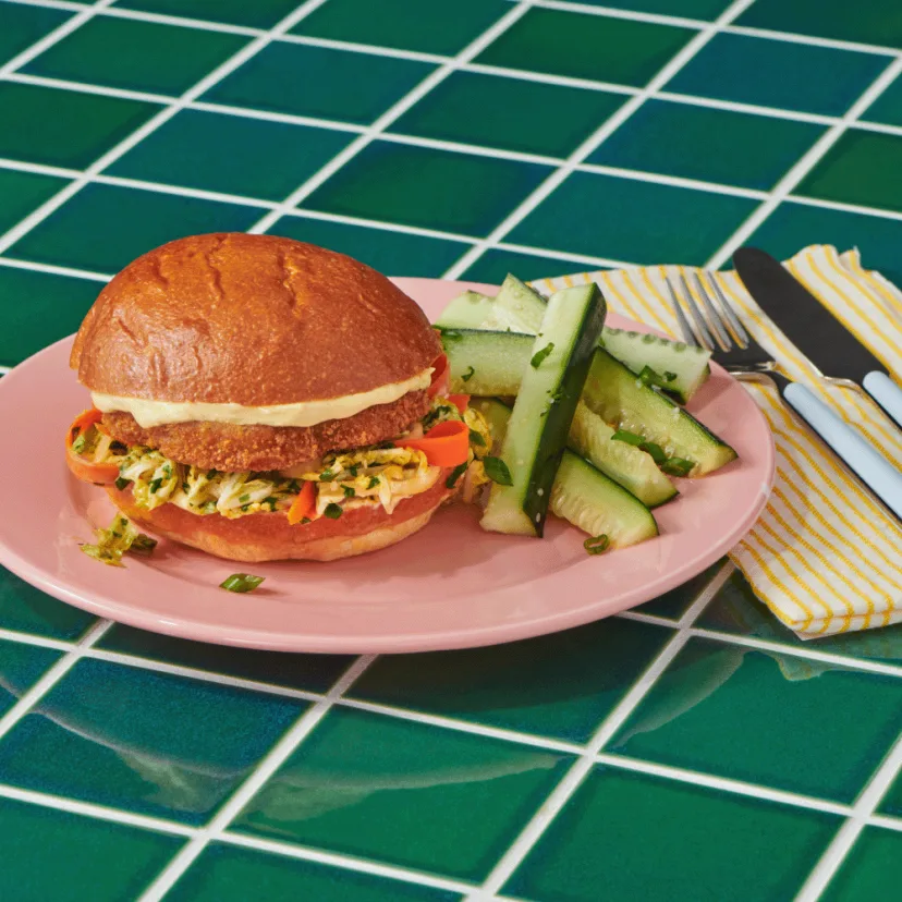 Impossible™ Chicken Patty Katsu Sandwich with napa cabbage slaw and curry mayo on a burger bun, served with a cucumber salad. 