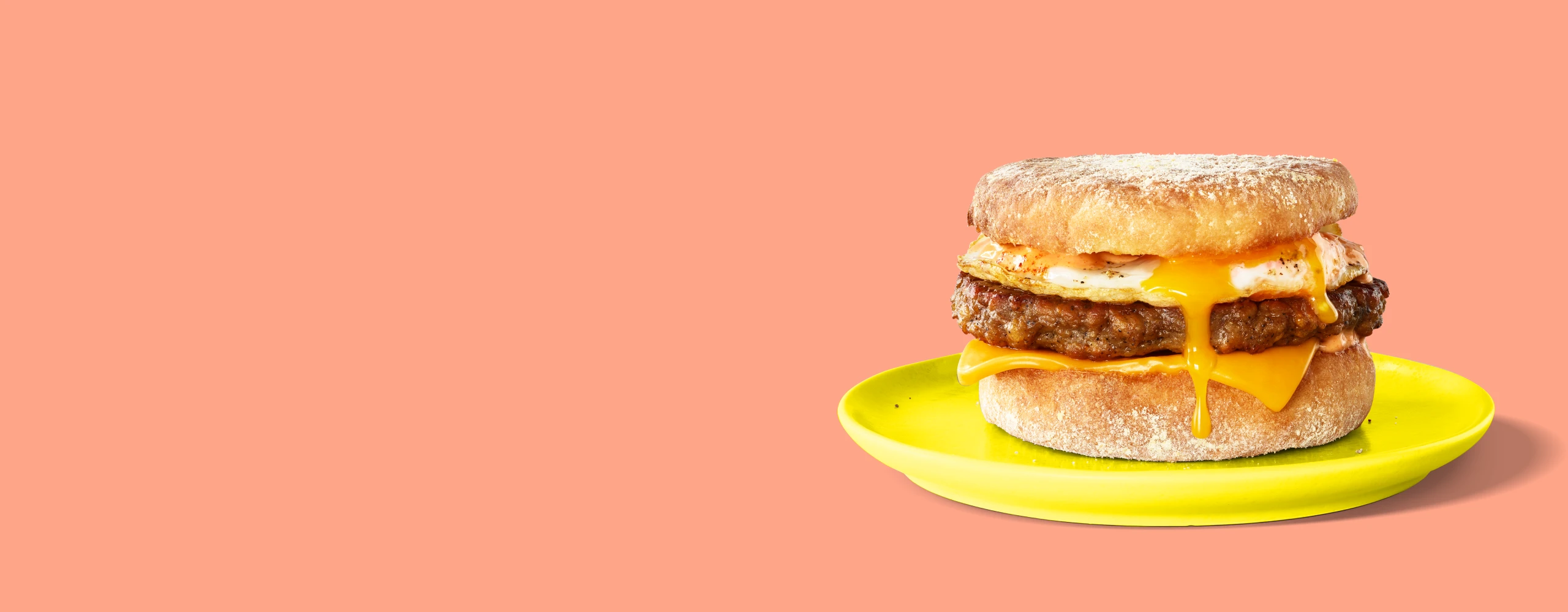 Impossible sausage breakfast sandwich with melty cheese and egg on a plate on a pink background