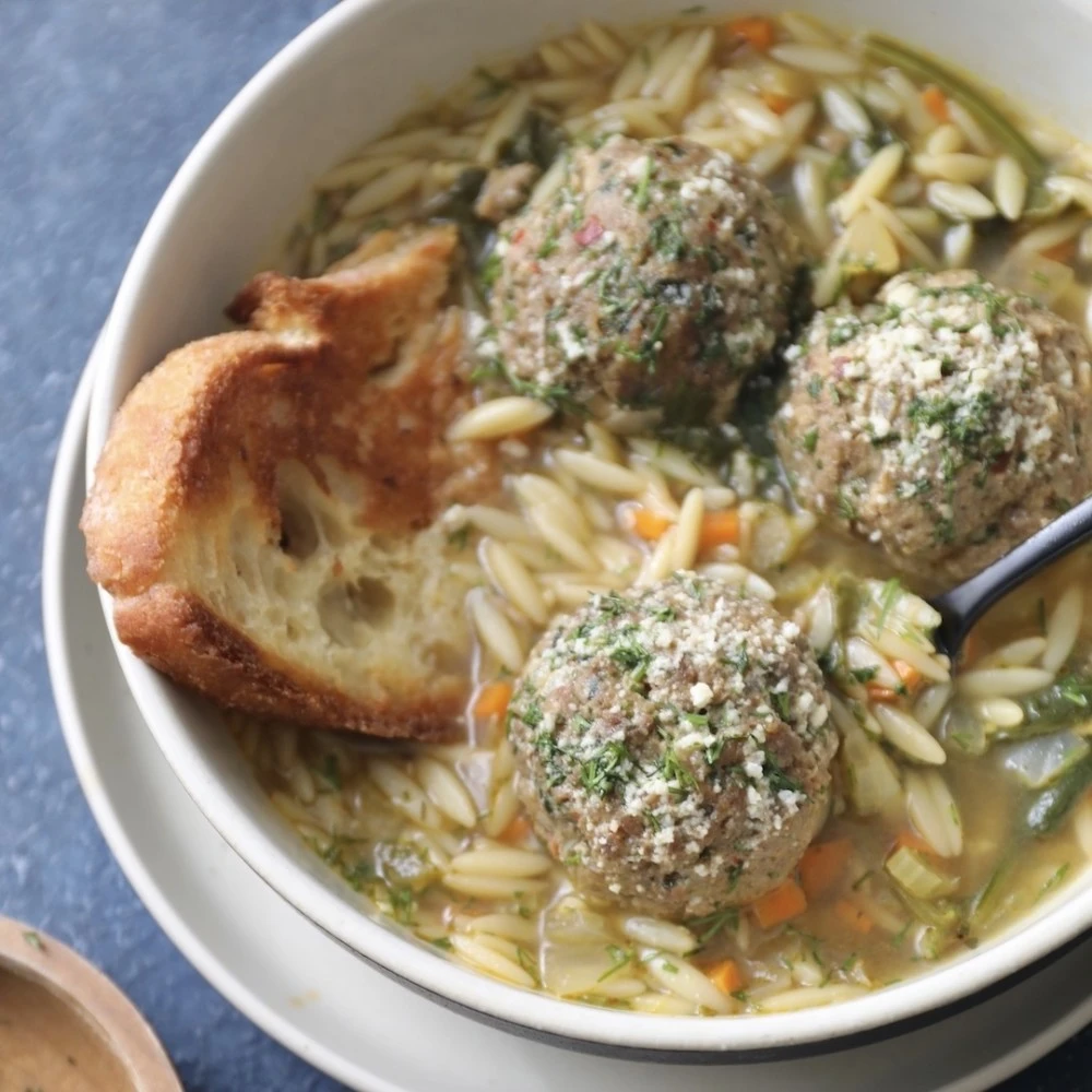 A large bowl of Impossible Italian Wedding Soup made with Impossible Italian Meatballs, orzo, parmesan cheese, and toasted bread. 