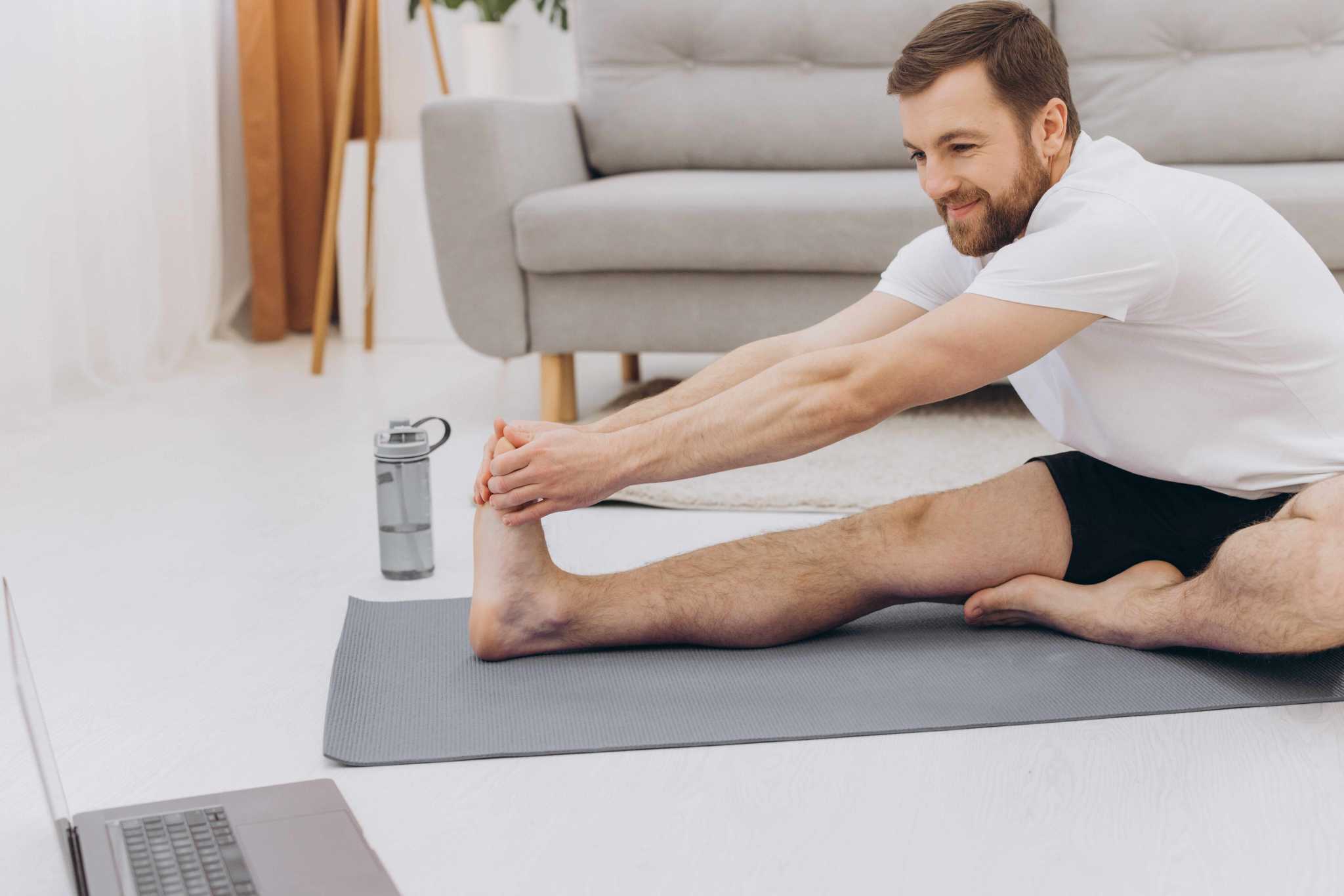 Image of man sitting on the ground with one leg out in front of him to perform a seated hamstring stretch. 