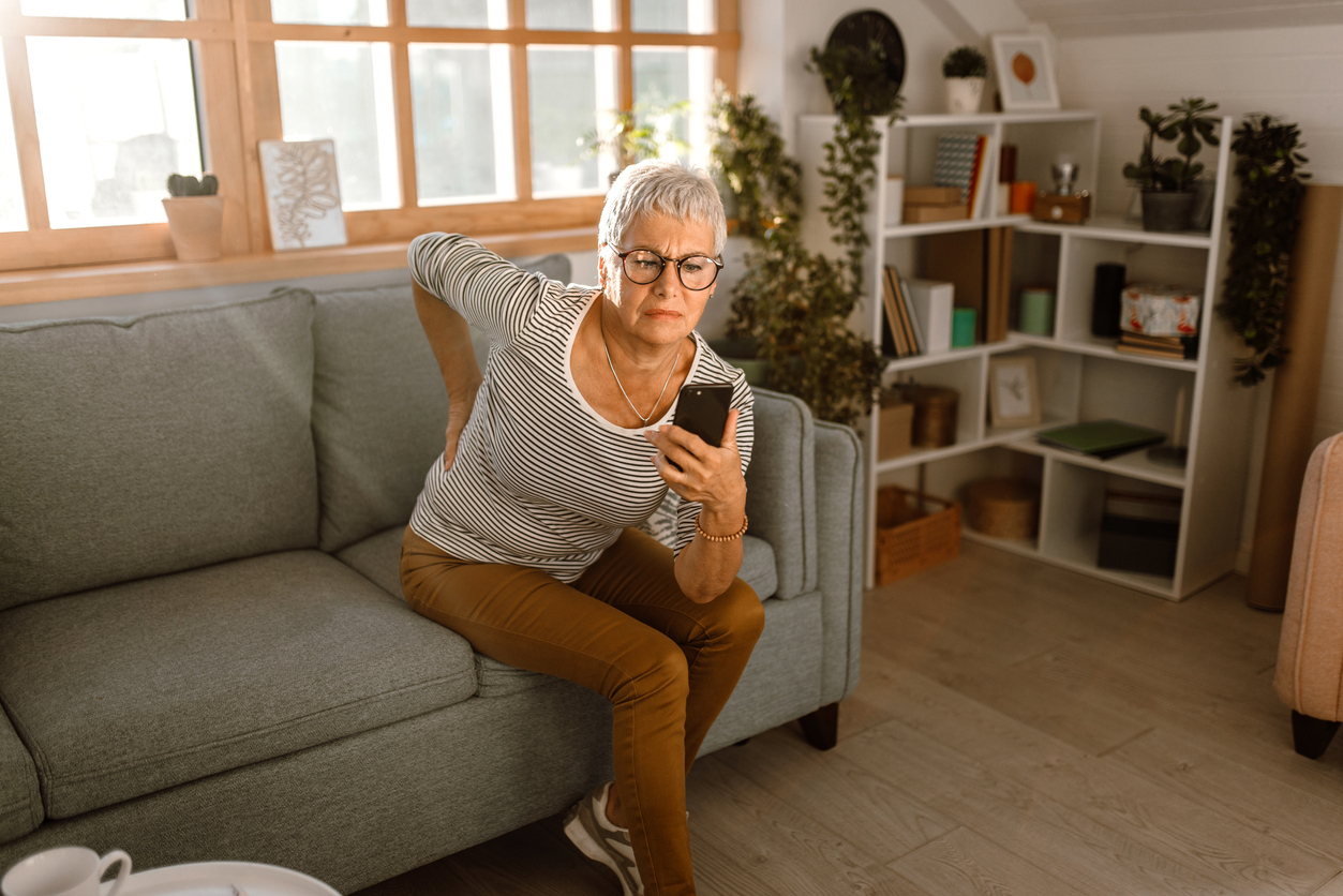 woman holding phone and her back because of back pain